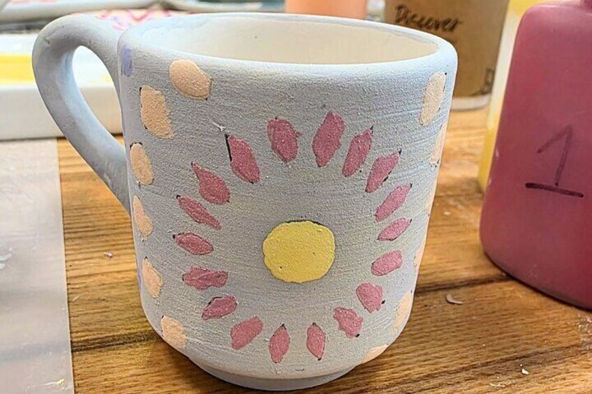 A mug with a painted design of leaves and a yellow circle. 2