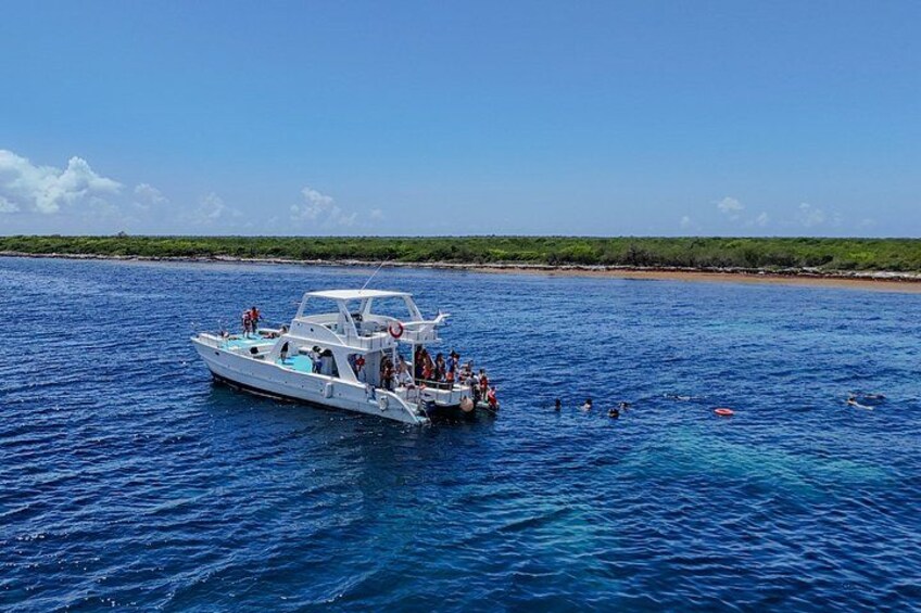 A white boat with people on board and swimmers in the water. 3