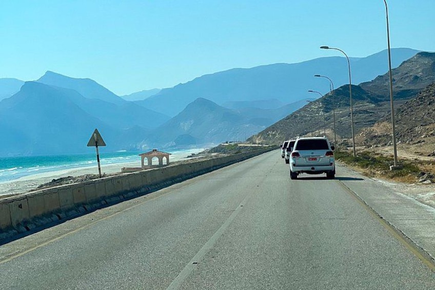 A coastal road with a white van, mountains in the background, and a beach on the left. 4