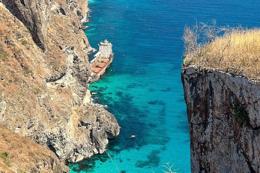 A ship near a rocky coastline with clear blue water. 1