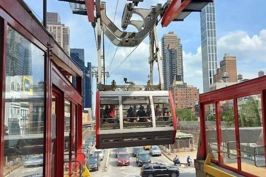 A cable car suspended between buildings, a busy street below, and a cityscape in the background. 1