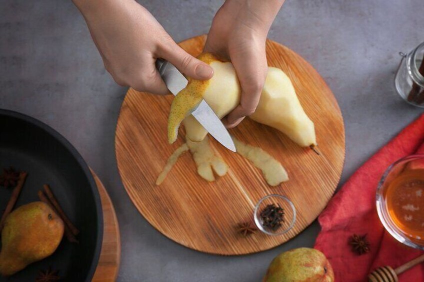A person peeling a potato on a wooden cutting board. 2