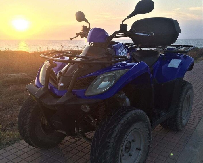 Un quad bleu est garé sur un chemin goudronné, avec un coucher de soleil en arrière-plan. 2