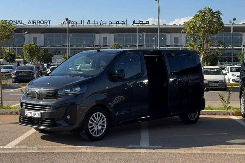 A black van parked in a lot with a building labeled 'NATIONAL AIRPORT' in the background. 2