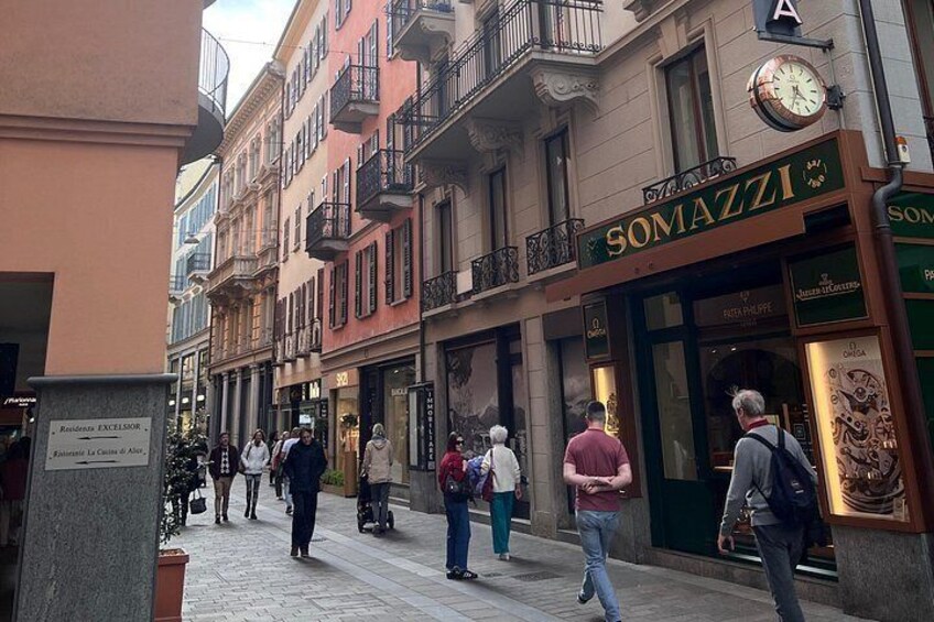 Calle con gente caminando, un reloj y una tienda llamada 'SOMAZZI'. 5