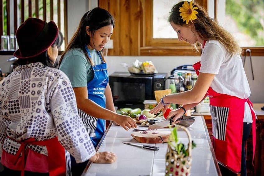 Three people preparing food in a kitchen with wooden cabinets and a window. 1