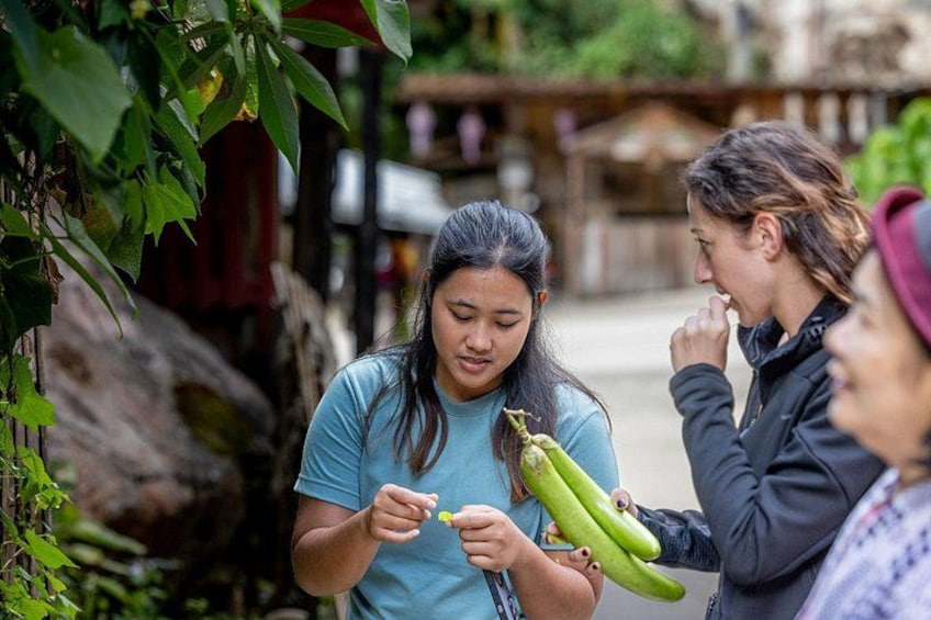 A person holding a bunch of green bananas, another person holding a small yellow object, and a third person observing. 4