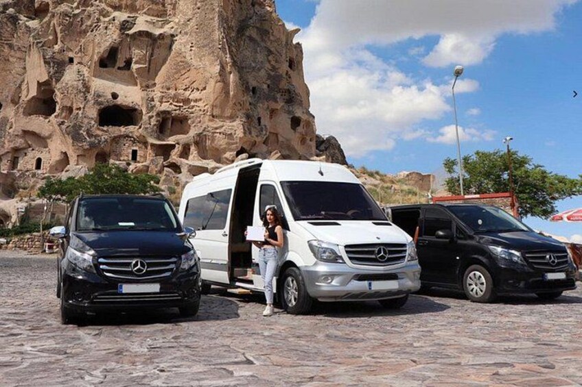Three cars parked in front of a rocky cliff with cave-like openings. 1