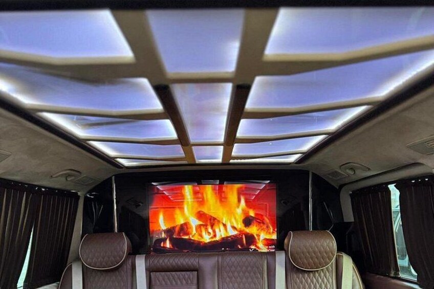 A vehicle interior with a large screen displaying a fire, overhead lighting, and leather seats. 5