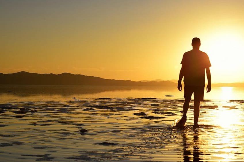 Une personne se tient dans une eau peu profonde au coucher du soleil, avec des montagnes en arrière-plan. 3