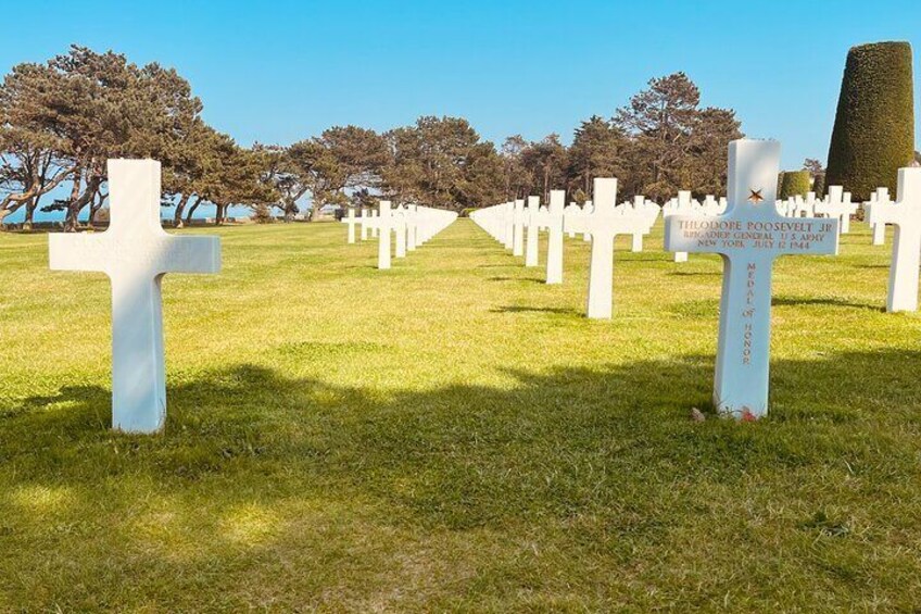 Un cimetière avec des croix blanches et une grande croix sur laquelle est fixée une plaque portant un nom. 1