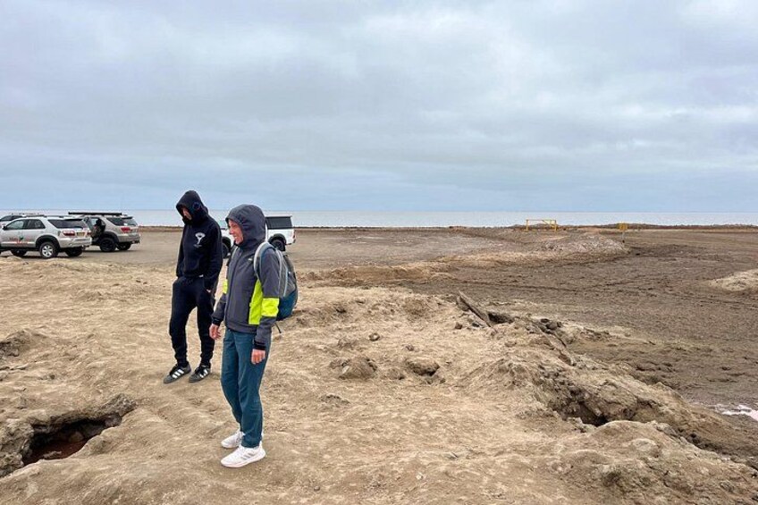 Two people standing on a sandy beach with vehicles in the background. 5