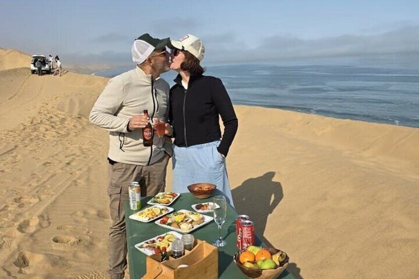 A couple on a picnic table with food and drinks on a beach. 1