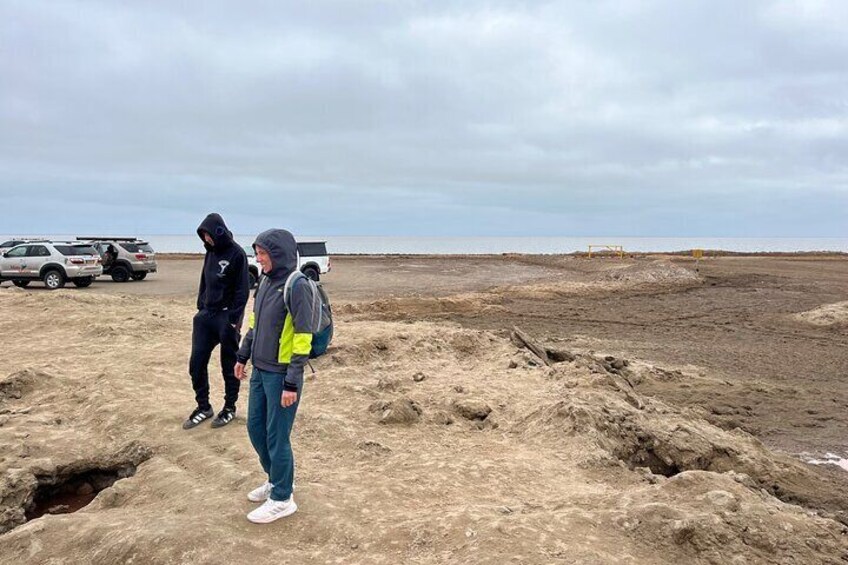 Two people standing on a sandy beach with vehicles in the background. 5