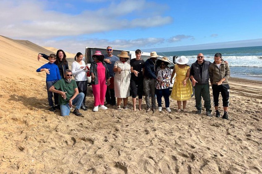 A group of people standing on a sandy beach with a vehicle and ocean in the background. 4