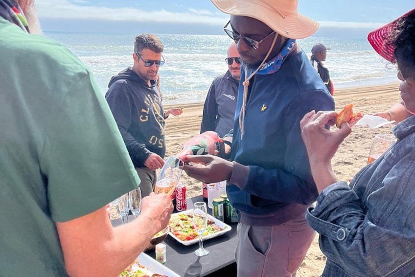 A group of people dining at a beachside table with food and drinks. 3
