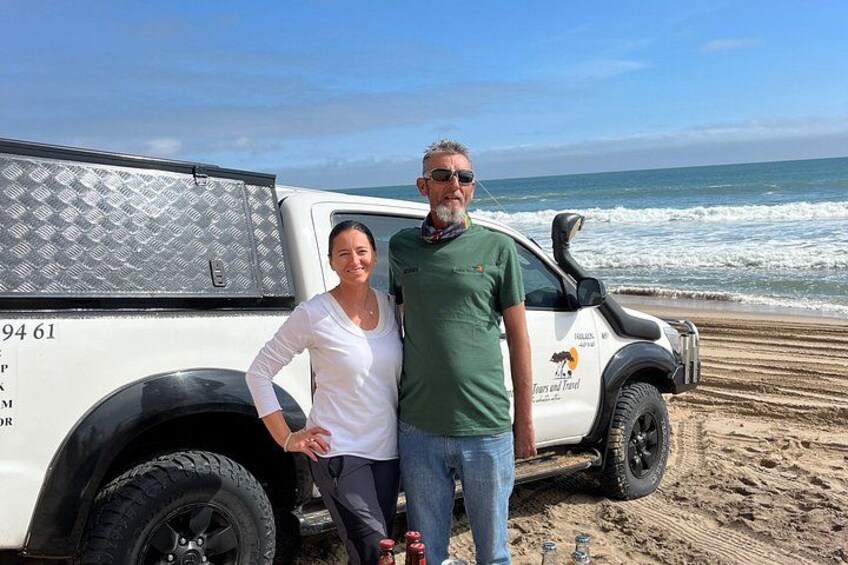 A white truck with a logo on the side parked on a sandy beach with the ocean in the background. 2