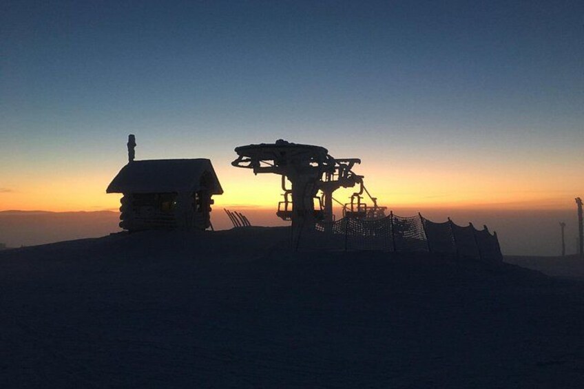 A mountain lodge at sunset with a ski lift in the foreground. 1