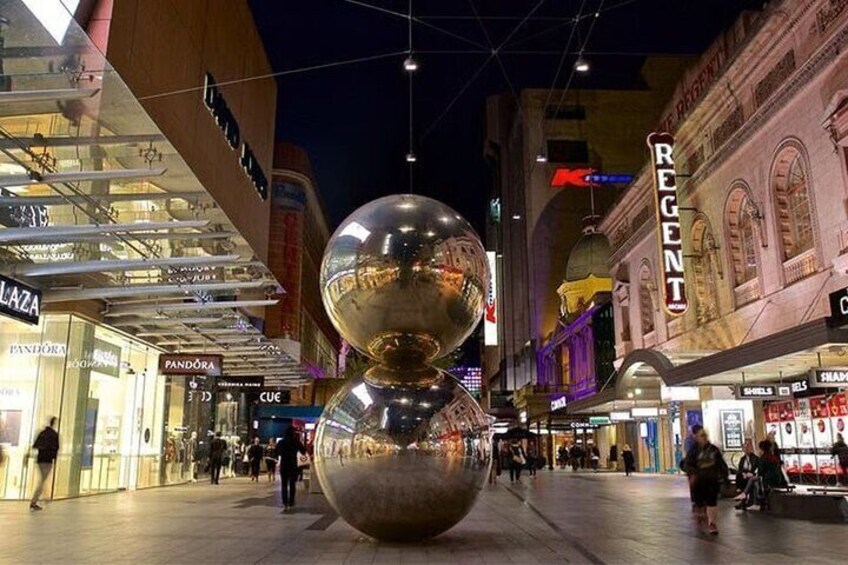 Un centro commerciale con una grande scultura sferica al centro, circondato da diversi negozi, tra cui Pandora. 1