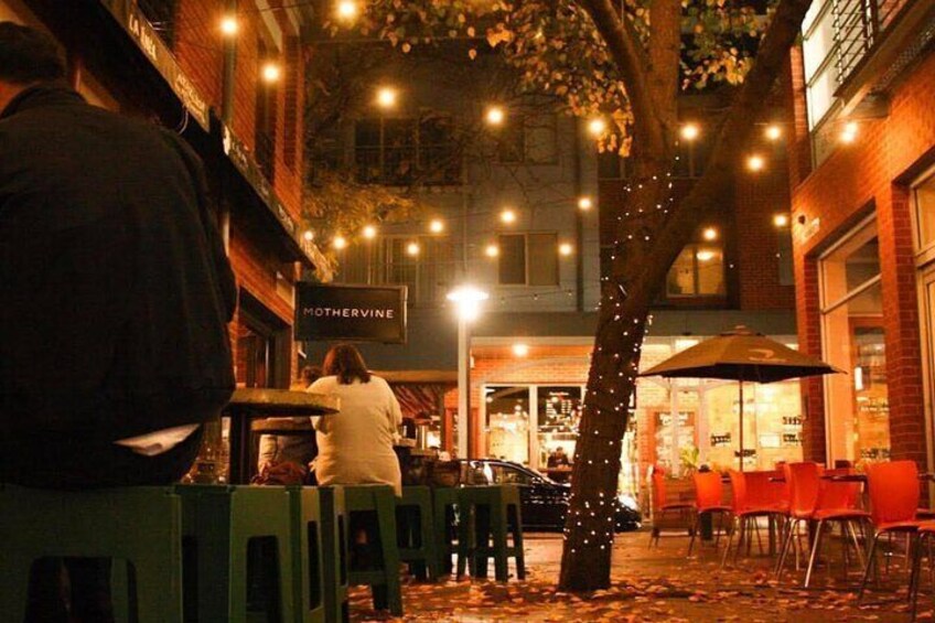 Un caffè all'aperto con tavoli e sedie, un albero illuminato e un cartello con la scritta 'Mothervine'. 5