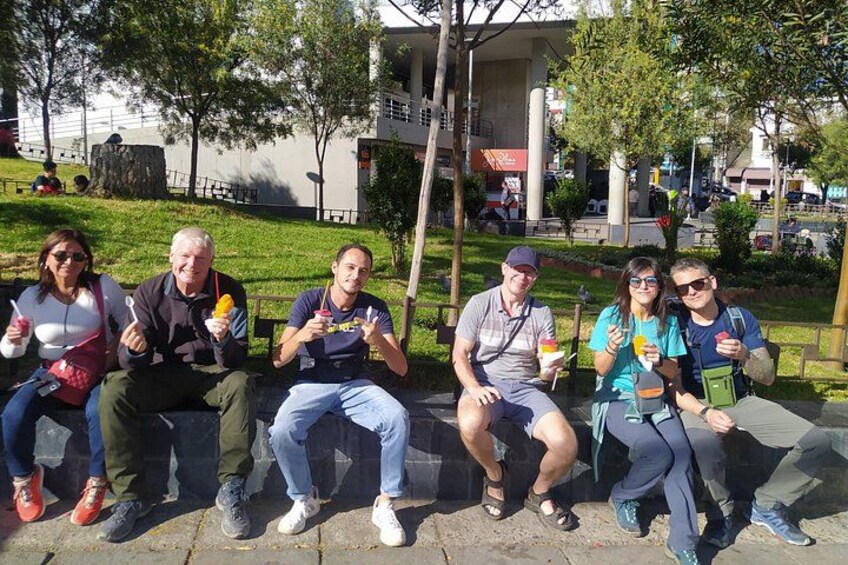 En grupp människor sitter på en bänk i en park och äter glass. 3