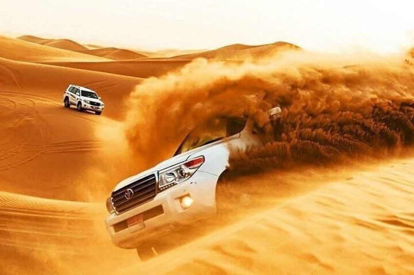 A white SUV driving through a desert with sand being kicked up by the vehicle. 1