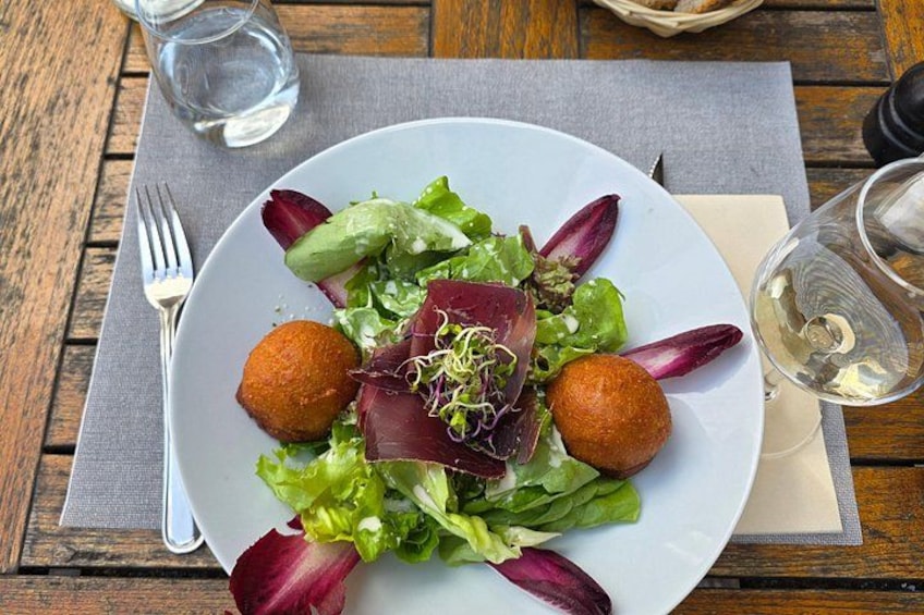 A plate of salad with greens, purple leaves, and two round items, possibly meatballs, on a wooden table with a fork and a glass of water. 5