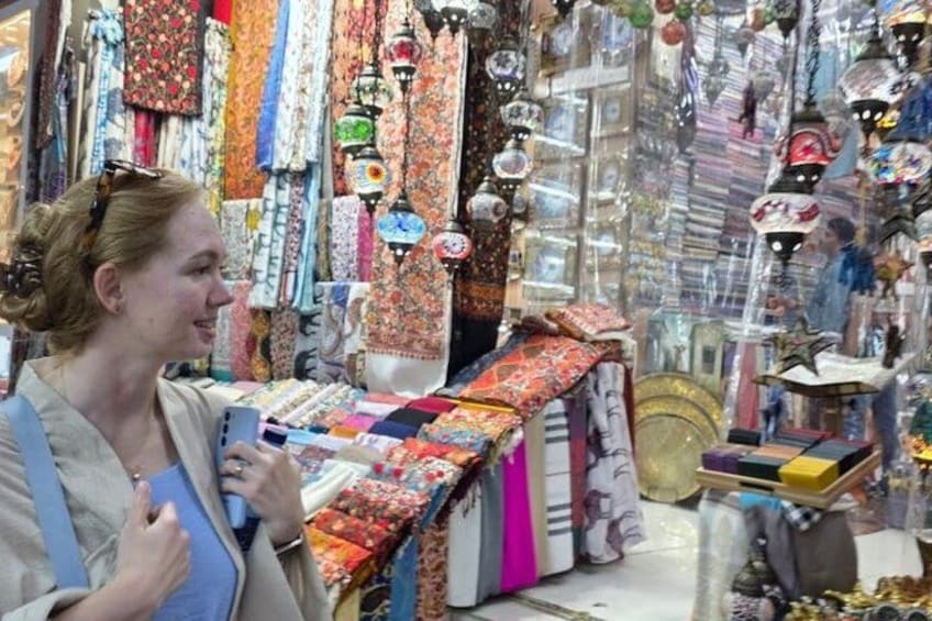 Una persona observa textiles en un mercado, con diferentes telas y adornos colgantes. 5