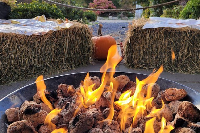 A campfire with burning wood, hay bales, and a pumpkin in the background. 3