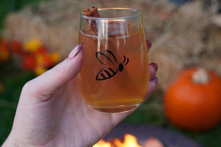 A hand holding a glass with a cinnamon stick and a logo. 1