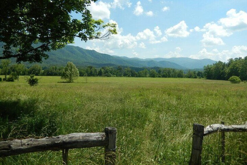 A grassy field with a wooden fence in the foreground and mountains in the background. 3