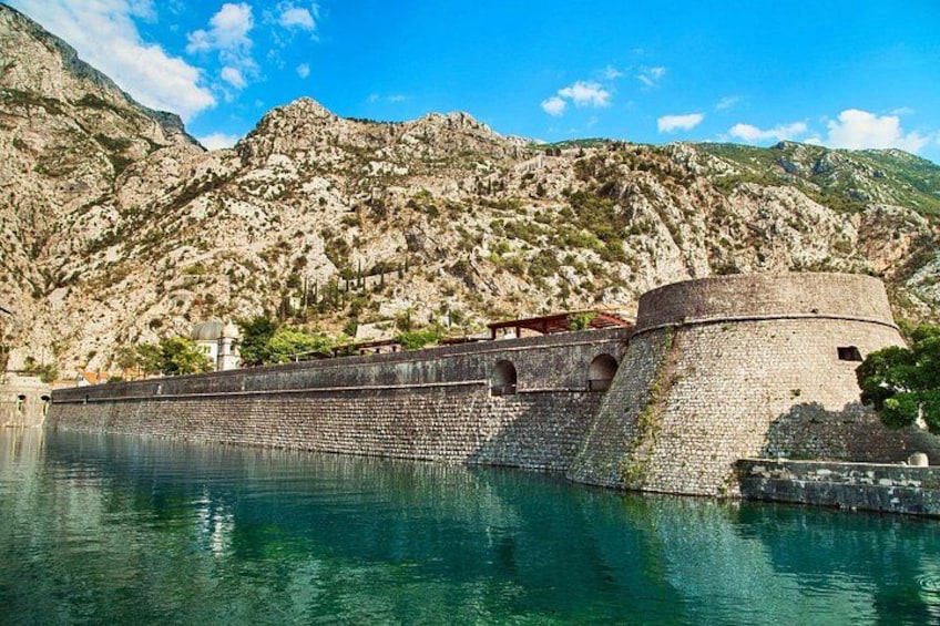 A historic stone fortress by a clear blue lake with rugged mountains in the background. 2