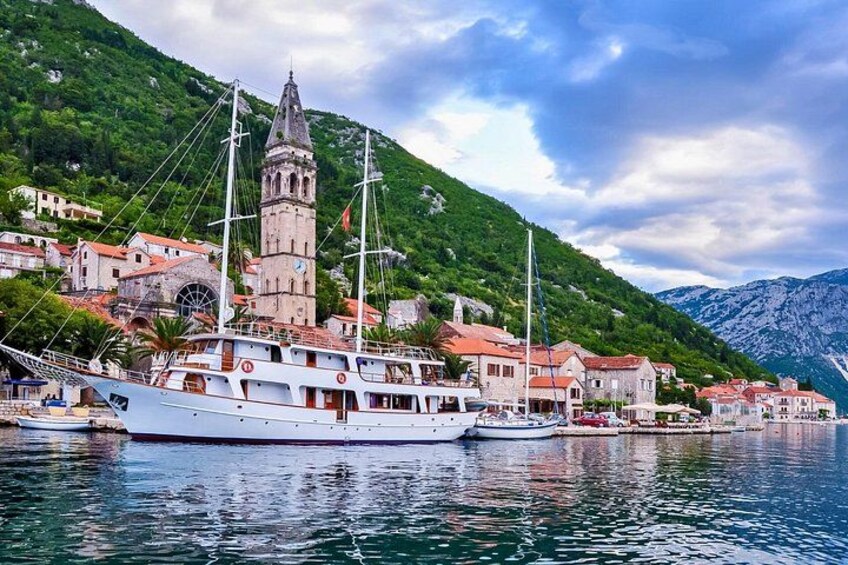 A coastal town with a prominent tower, boats docked along the waterfront, and lush green hills in the background. 3