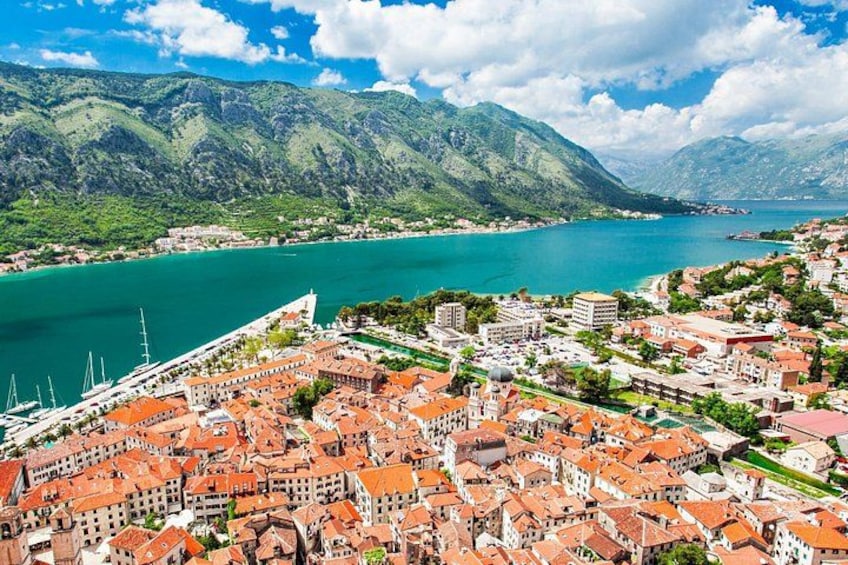 A coastal town with red-roofed buildings, a marina, and mountains in the background. 4