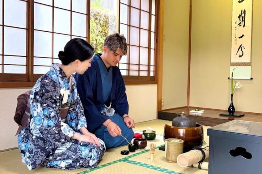 Two people in traditional Japanese attire sitting on tatami mats, with a tea ceremony setup including a teapot, cups, and a wooden table. 5
