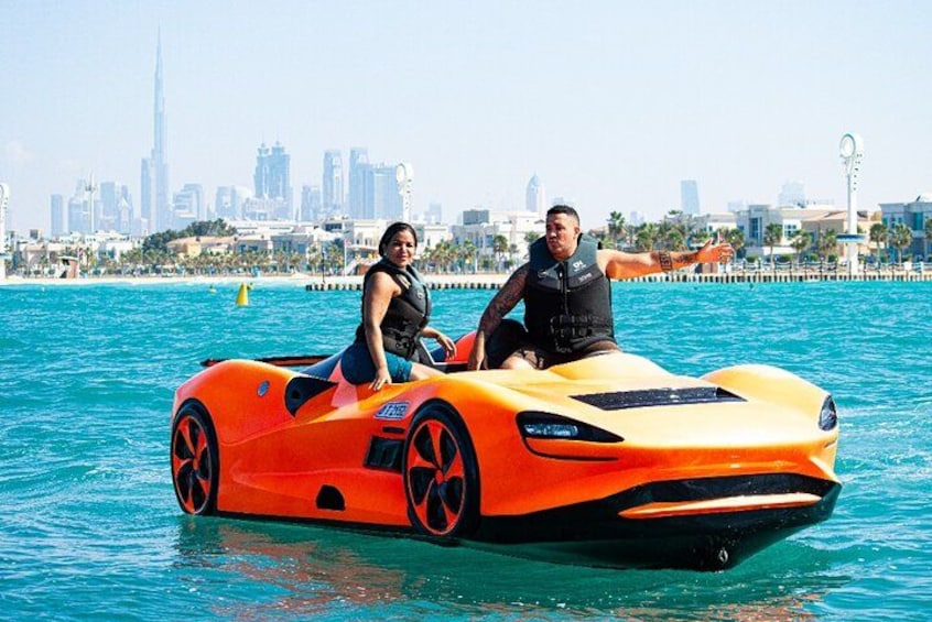 A couple on a bright orange watercraft in a body of water with a city skyline in the background. 1