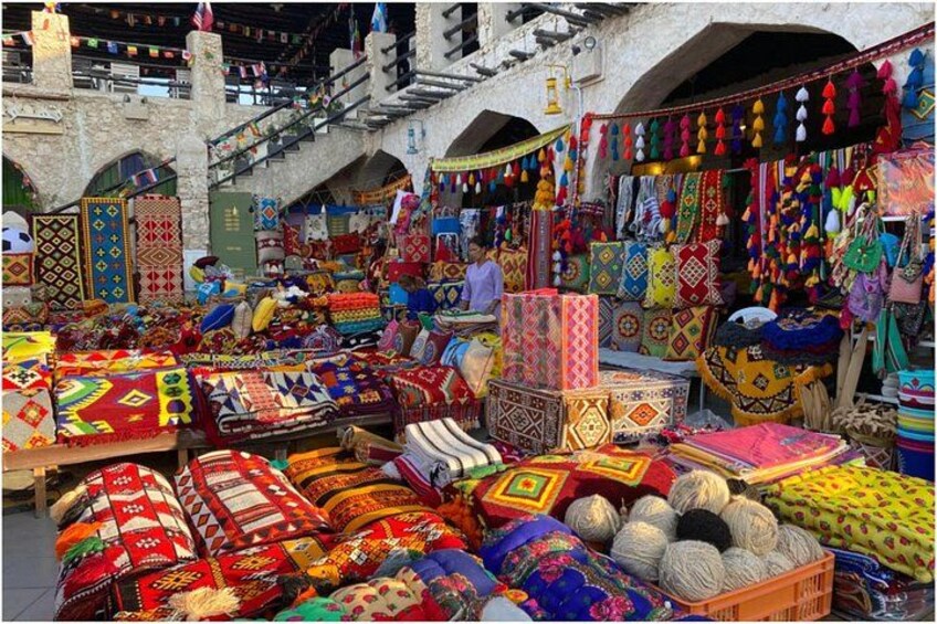 Een markt met kleurrijke textielwaren en tapijten, uitgestald op tafels en opgehangen aan het plafond. 3