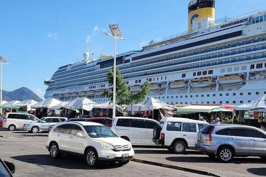 A cruise ship docked at a port with several cars parked in front. 4