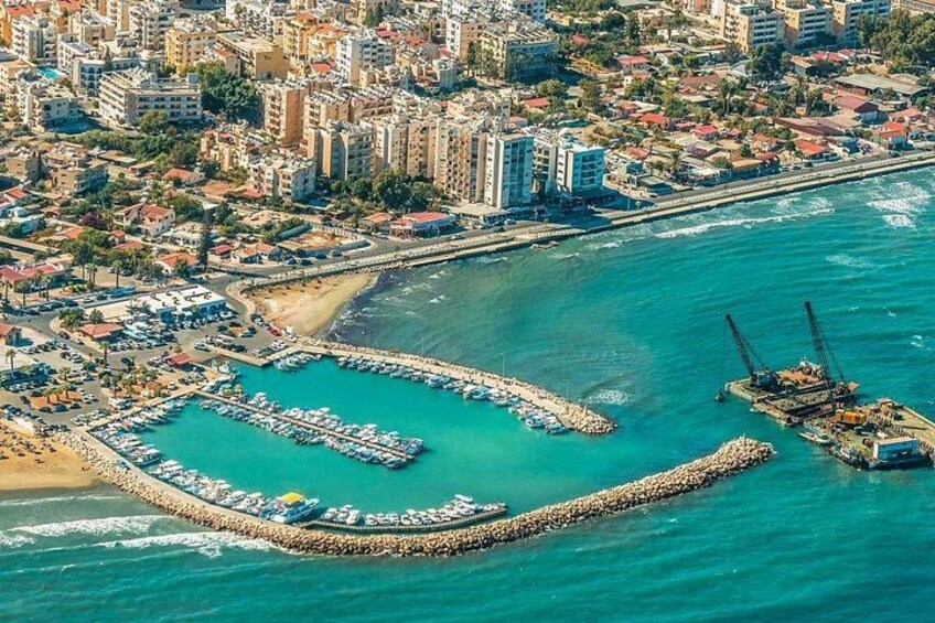 An aerial view of a coastal city with a marina, buildings, and a beach. 1