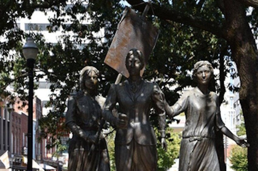 A statue of three figures, one holding a flag, in an outdoor setting with trees and a street lamp. 4