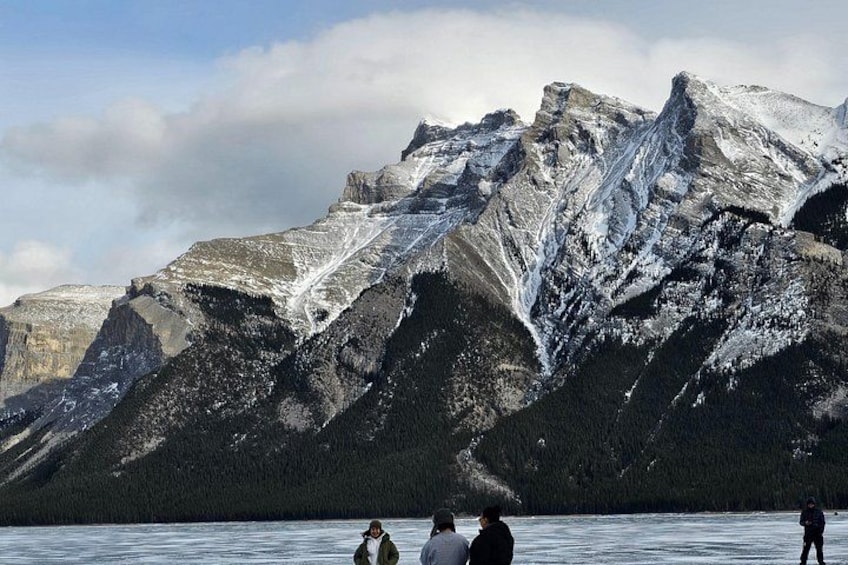 A group of people standing on a frozen lake with snow-covered mountains in the background. 1