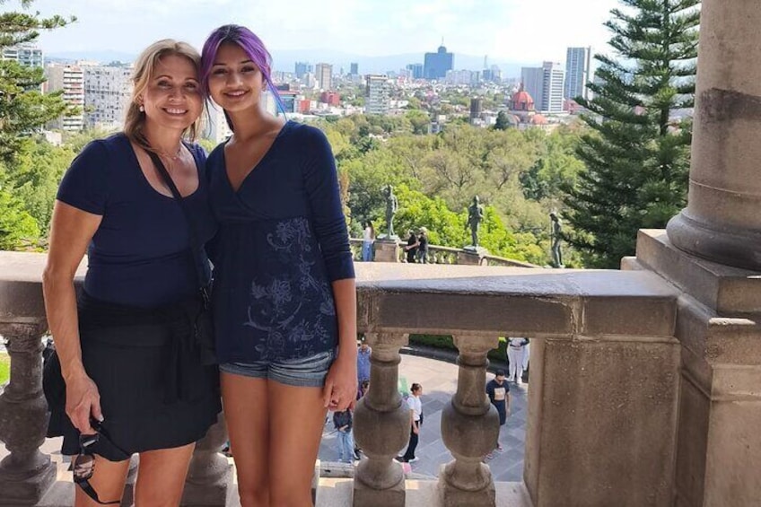 Deux personnes se tiennent sur un balcon, avec une vue sur la ville en arrière-plan. 1