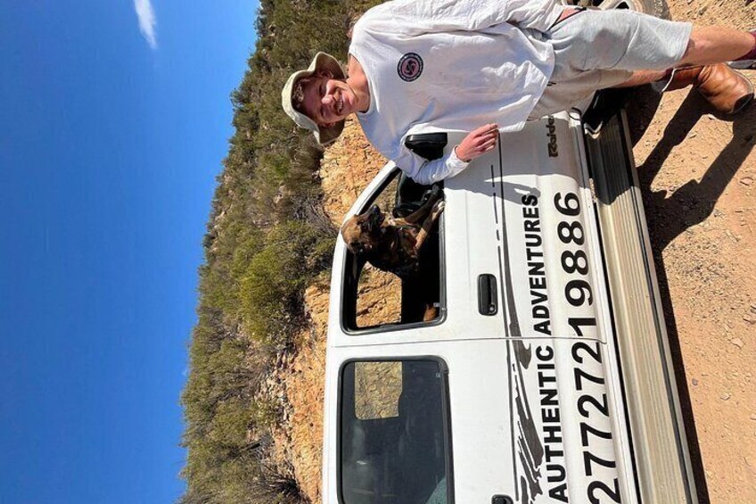 A person leaning on a vehicle with 'AUTHENTIC ADVENTURES' and a phone number on the side. 3