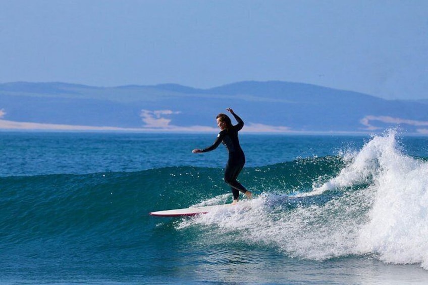 A person surfing on a wave with a clear sky and distant mountains in the background. 1