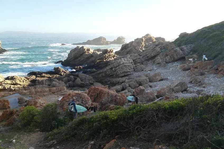 A rocky coastal landscape with surfers and their surfboards. 3