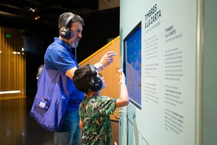 A person wearing headphones and a blue shirt standing next to a wall with text and a window. 5