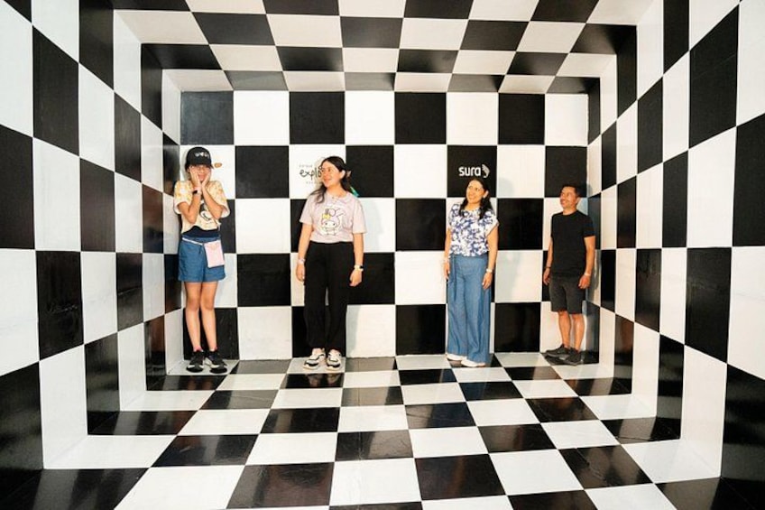 Four people standing in a checkered pattern on the floor with a black and white wall. 4