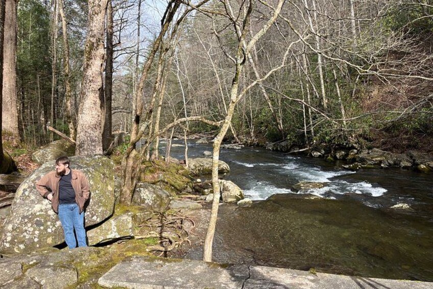 Una persona de pie sobre rocas junto a un río que fluye en un área boscosa. 2