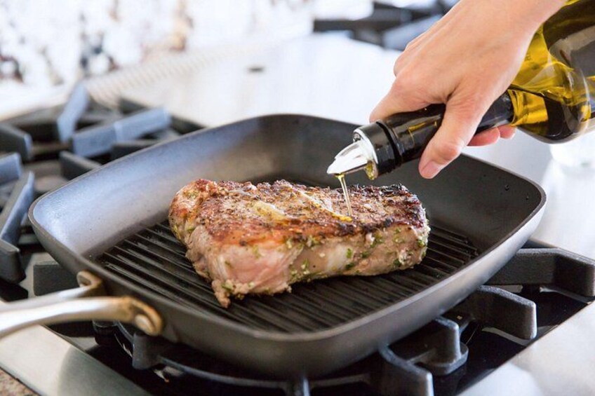En hånd hælder olie på en bøf på en grillpande. 4