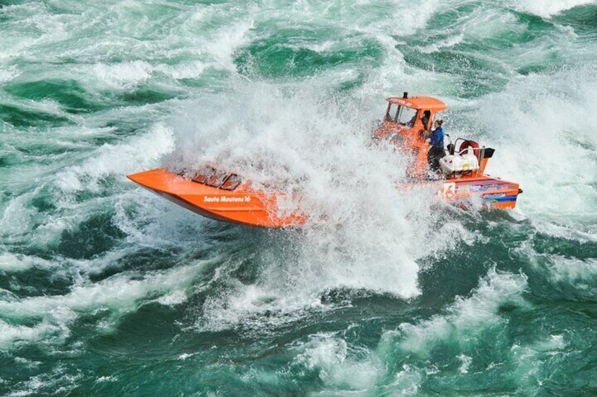 Un bote motorizado naranja con dos personas navegando por aguas agitadas. 2